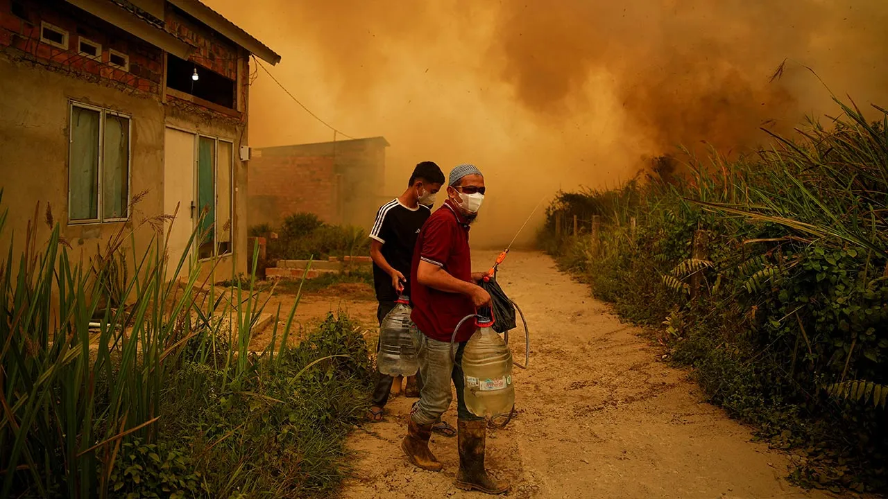 Residents carry containers of water as a wildfire burns near a residential area in Banyuasin, South Sumatra province, Indonesia, October 7, 2026. REUTERS/Abriansyah Liberto