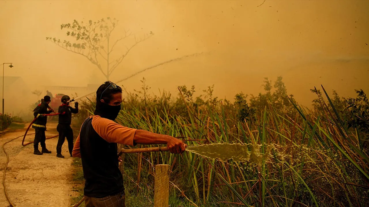 A resident sprays water to extinguish a wildfire near a residential area in Banyuasin, South Sumatra province, Indonesia, October 7, 2026. REUTERS/Abriansyah Liberto