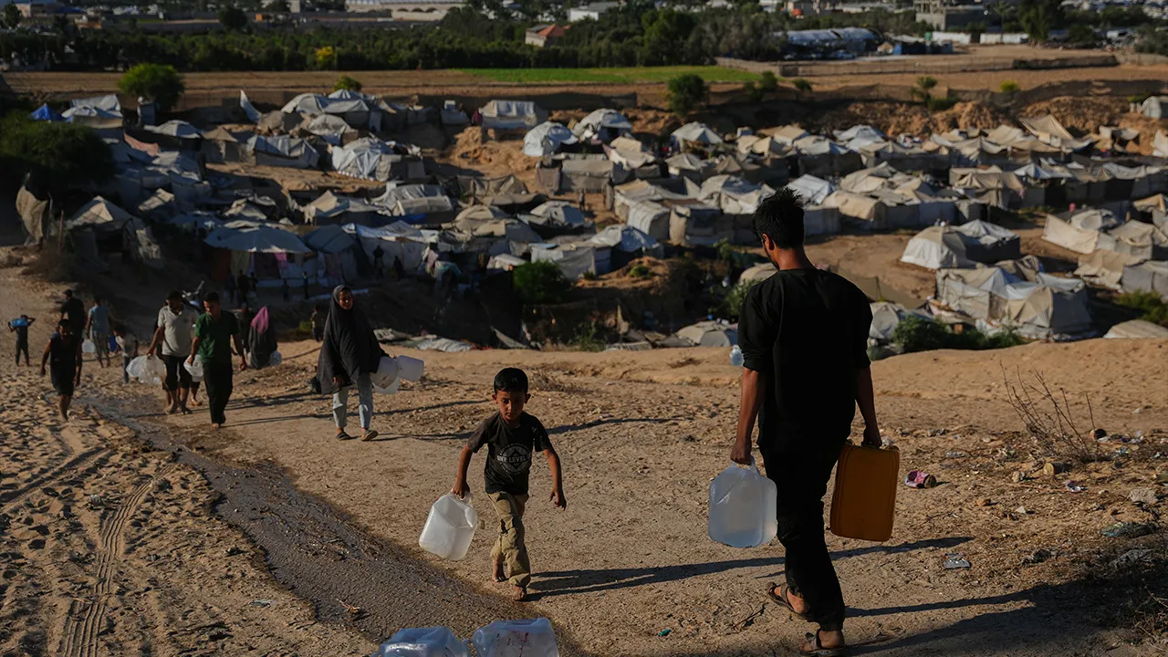 Displaced Palestinians carry water containers near a tent camp in Deir al-Balah, central Gaza Strip, Wednesday, Oct. 7, 2026. (AP Photo/Abdel Kareem Hana)