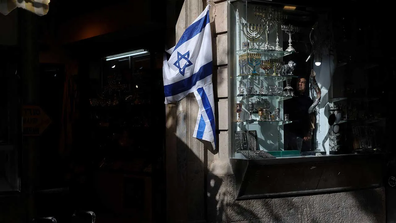 A shopkeeper looks out of his shop window displaying Judaica items, including ceremonial menorahs and shofars, just before closing time for Shabbat, four days before Israelis are due to hold a national election in Jerusalem on October 23, 2026. REUTERS/Kevin Coombs