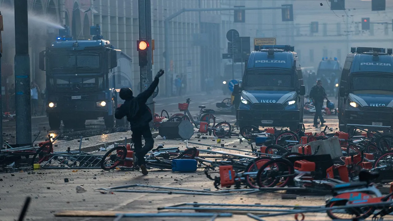 A masked demonstrator raises an arm in front of police vehicles during clashes following a protest against the rising cost of living in Bologna, Italy, October 17, 2026. REUTERS/Michele Lapin