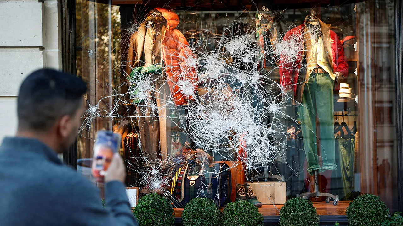 A man takes photos of a vandalised Ralph Lauren storefront a day after clashes during a national day of demonstrations against the cost of living and rising fuel prices, in Paris, France, October 18, 2026. REUTERS/Benoit Tessier
