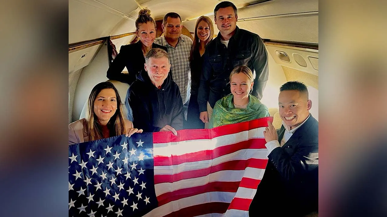 Stephen Hubbard, a 74-year-old US citizen held in Russian custody since 2022, poses with family members and US officials aboard a flight to the United States after his release from prison, in this handout photograph released on October 21, 2026. US Government/Handout via REUTERS. BEST QUALITY AVAILABLE.
