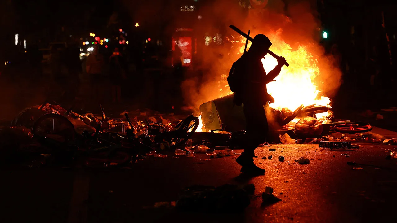 A person walks as flames rise during civil unrest, the day after a national day of demonstrations against the cost of living and rising fuel prices, in Paris, France, October 18, 2026. REUTERS/Abdul Saboor